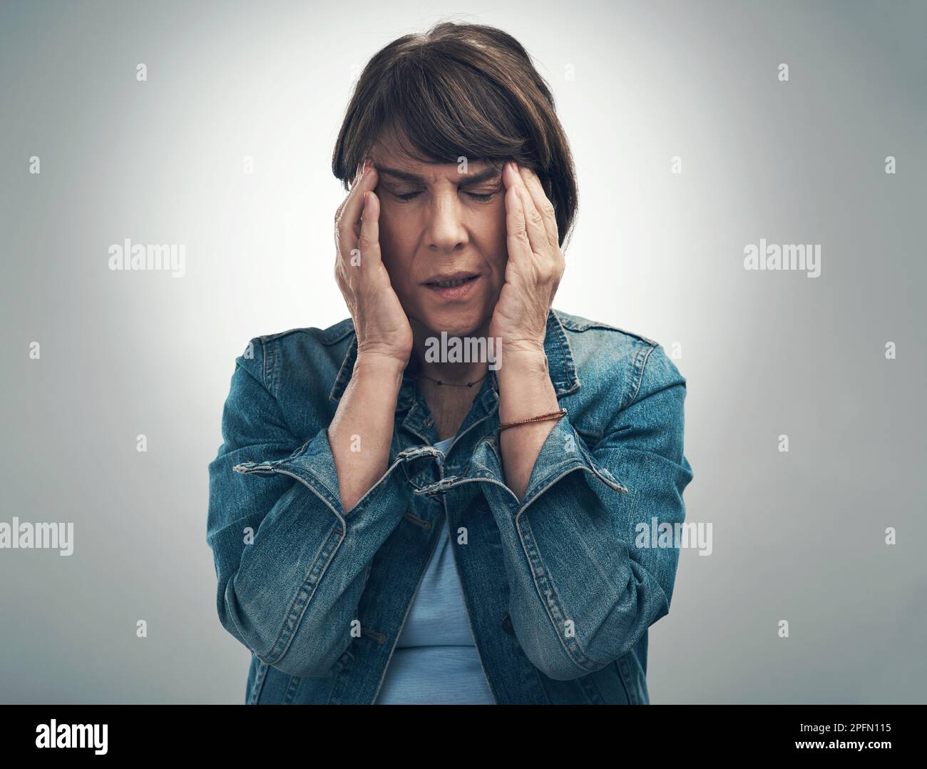 Désolé, migraine en cours - IM temporaire hors service. Photo en studio d'une femme âgée souffrant d'un mal de tête sur fond gris. Banque D'Images