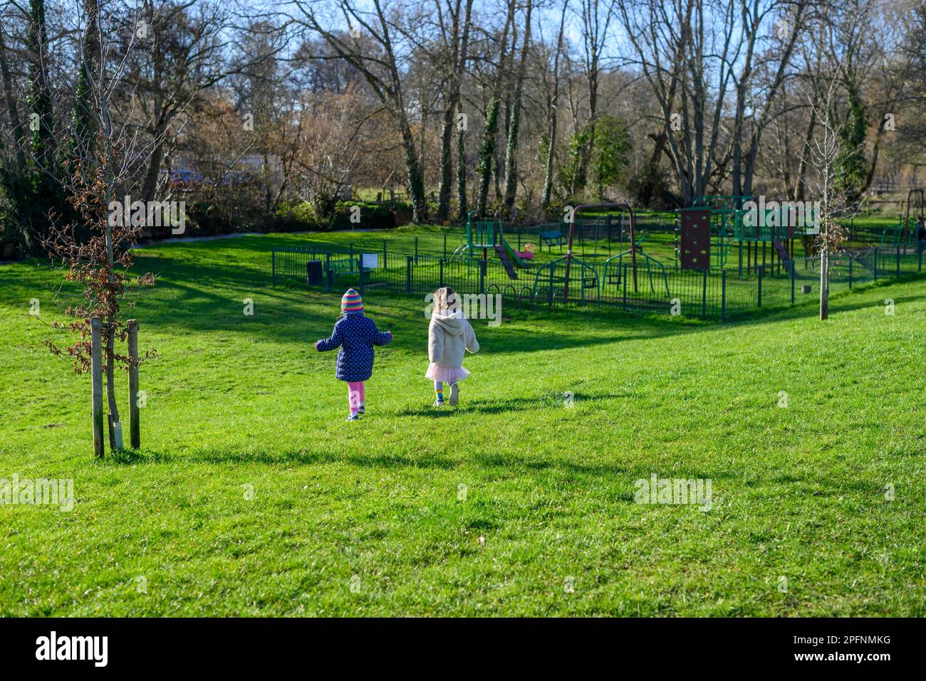 Les enfants qui s'exécutent sur l'herbe verte vers une aire de jeux Banque D'Images