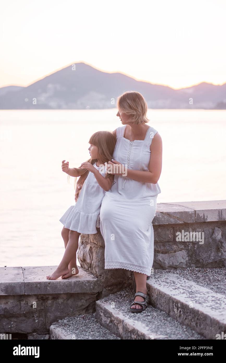 Mère enceinte du millénaire assis avec sa fille au coucher du soleil au bord de la mer. Une femme d'âge moyen épouse une petite fille. Le voyage d'un seul parent. Grossesse en santé Banque D'Images