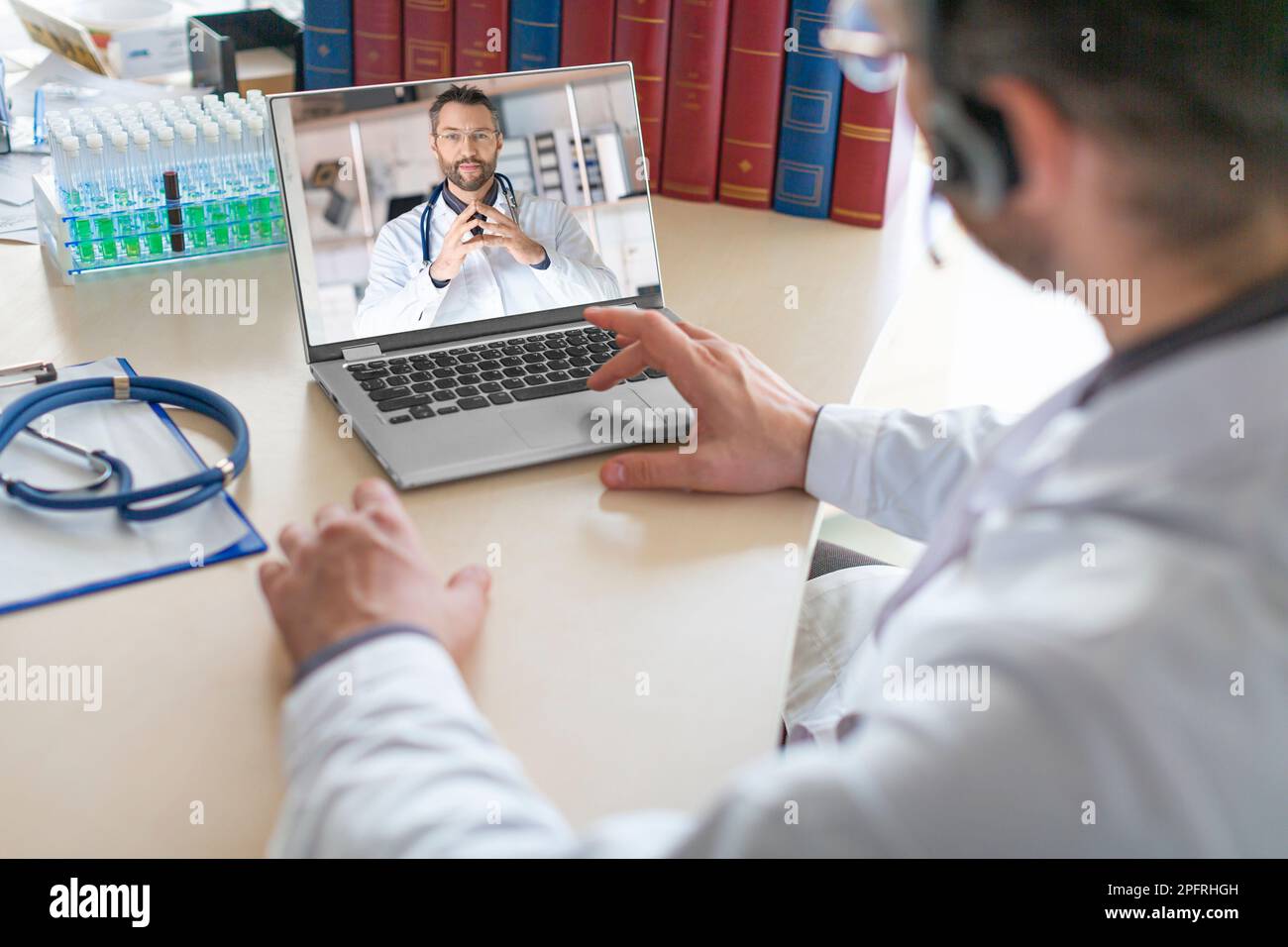 Un médecin s'assoit dans son bureau médical et mène une consultation virtuelle avec un collègue à l'aide d'un ordinateur portable. Les médecins discutent du medi d'un patient Banque D'Images