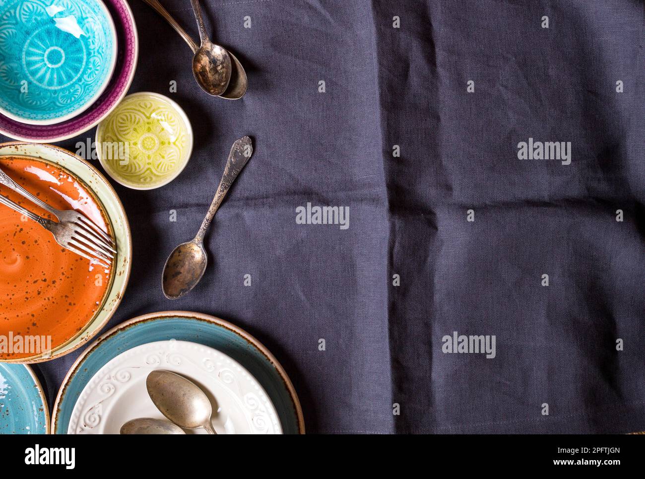 Assiettes et bols vides multicolores vintage sur une nappe en lin gris. Avec cuillères et fourchettes anciennes. Espace pour le texte. Réglage de la barre de coupe. En délabeur Banque D'Images
