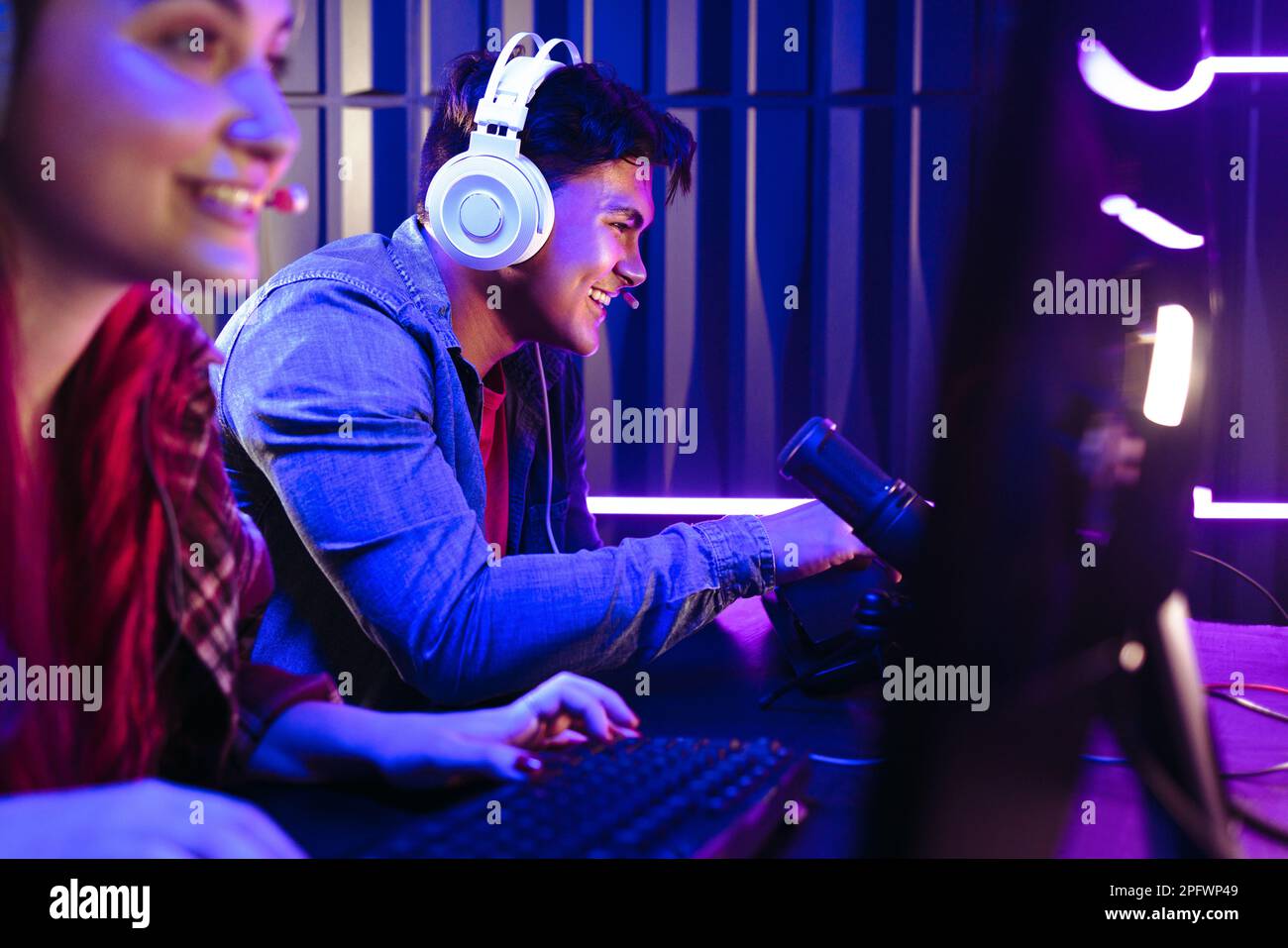 Gamers Gen Z se disputant dans un jeu vidéo en ligne, avec un microphone pour enregistrer en direct la compétition sur une plate-forme de streaming. Deux jeunes heureux jouent Banque D'Images