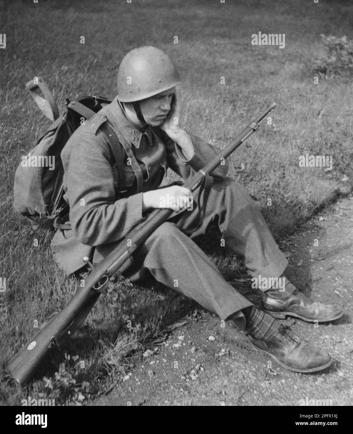 Soldat en 1940s. Un homme dans son uniforme, son fusil et sa parcelle semble fatigué quand il est assis sur le sol, reposant sa tête sur son bras. Suède 1942 Banque D'Images