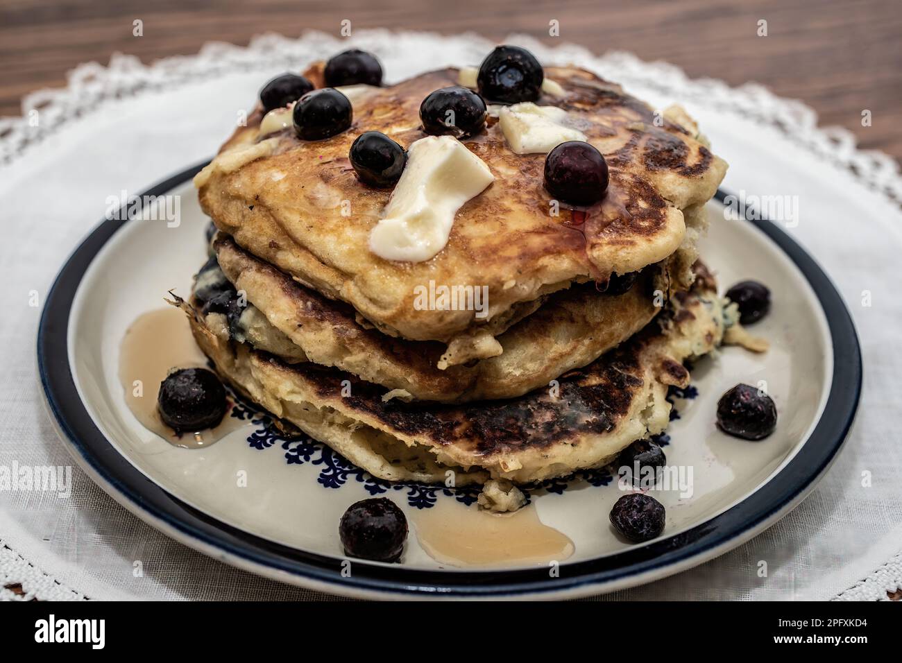 Une pile de crêpes aux myrtilles au babeurre avec du beurre et du sirop pour un repas de petit-déjeuner sur une assiette de médaillons sur un napperon blanc; Taylors Falls, Minnesota, États-Unis. Banque D'Images