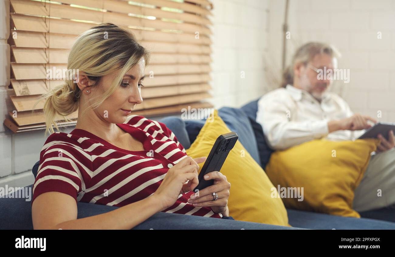 Dépendance de gadgets. père et dauther tenant et utilisant différents appareils électroniques tout en étant assis sur le canapé dans la salle de séjour à la maison. Banque D'Images