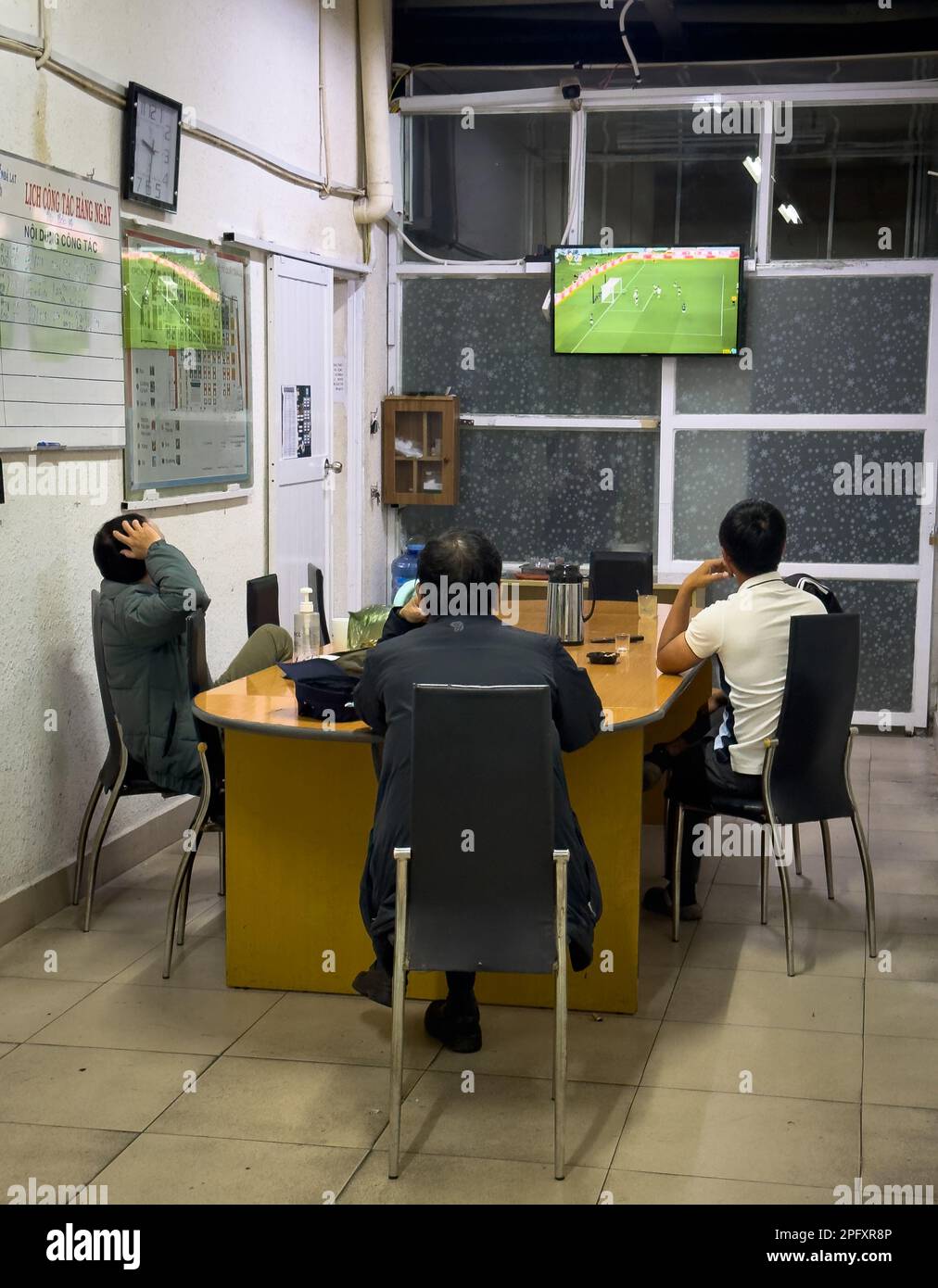 Trois gardes de sécurité du marché de Dalat au Vietnam s'assoient pour assister à un match de football à la télévision qui aura lieu lors de la coupe du monde de la FIFA 2022. Banque D'Images