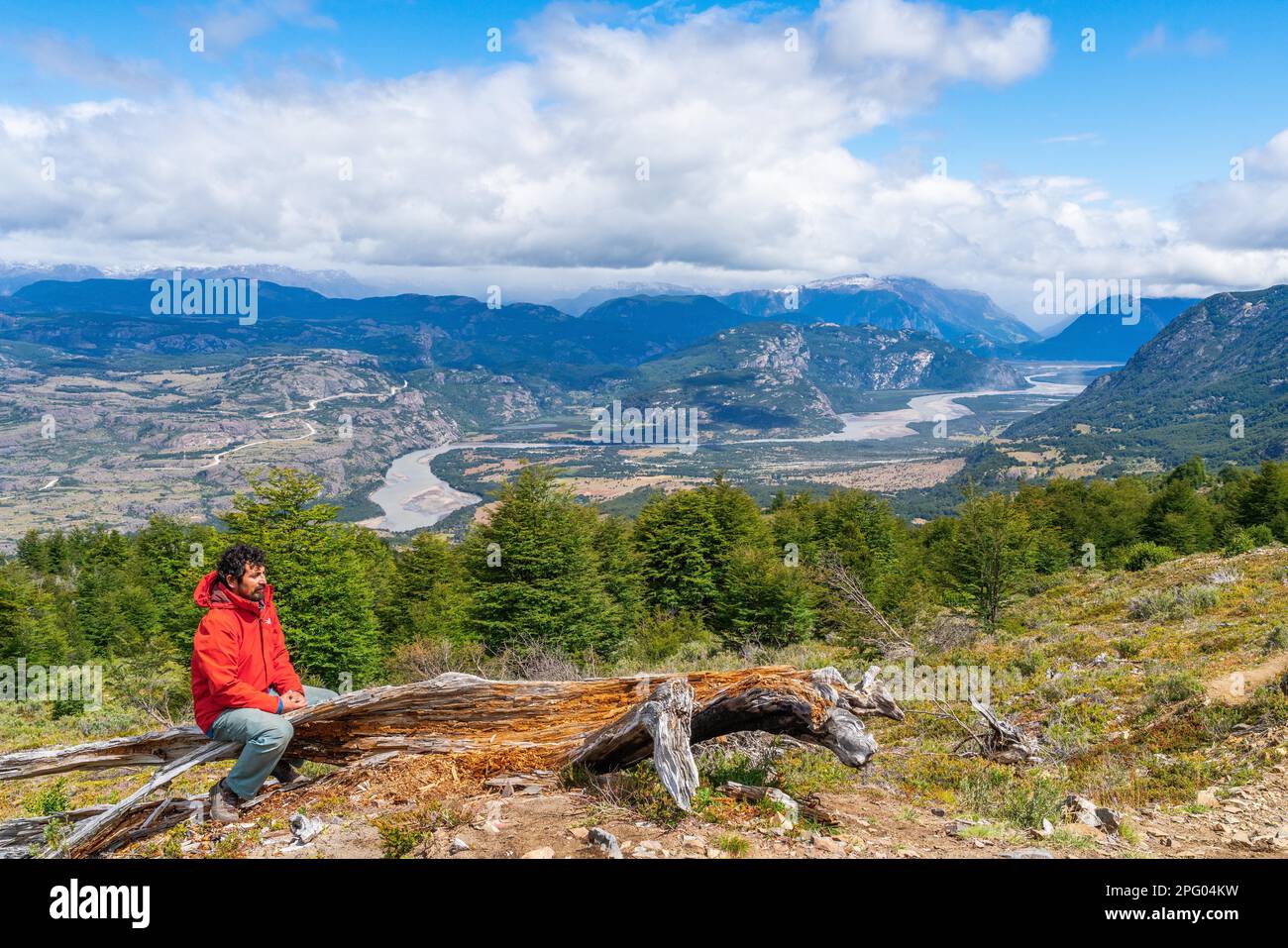 Randonneur prenant une pause sur un tronc d'arbre, montée à la lagune sur Cerro Castillo montagne, la vallée de la rivière du Rio Ibanez dans le fond, Cerro Banque D'Images