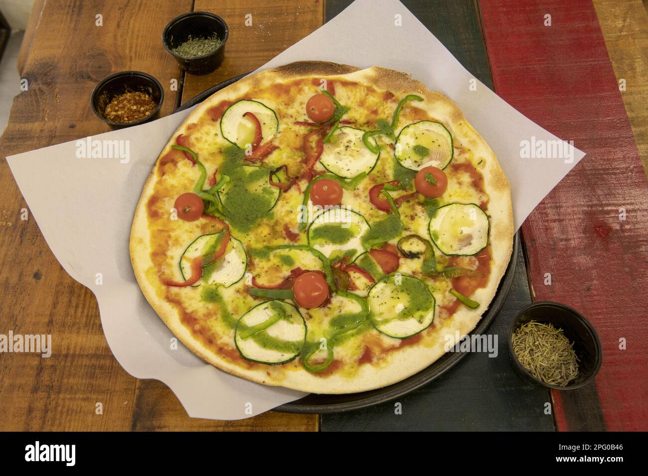 Une merveilleuse pizza à croûte mince moyenne avec différents types de légumes frais, tomates cerises, sauce au pesto et pomodoro sur une table en bois de couleur Banque D'Images