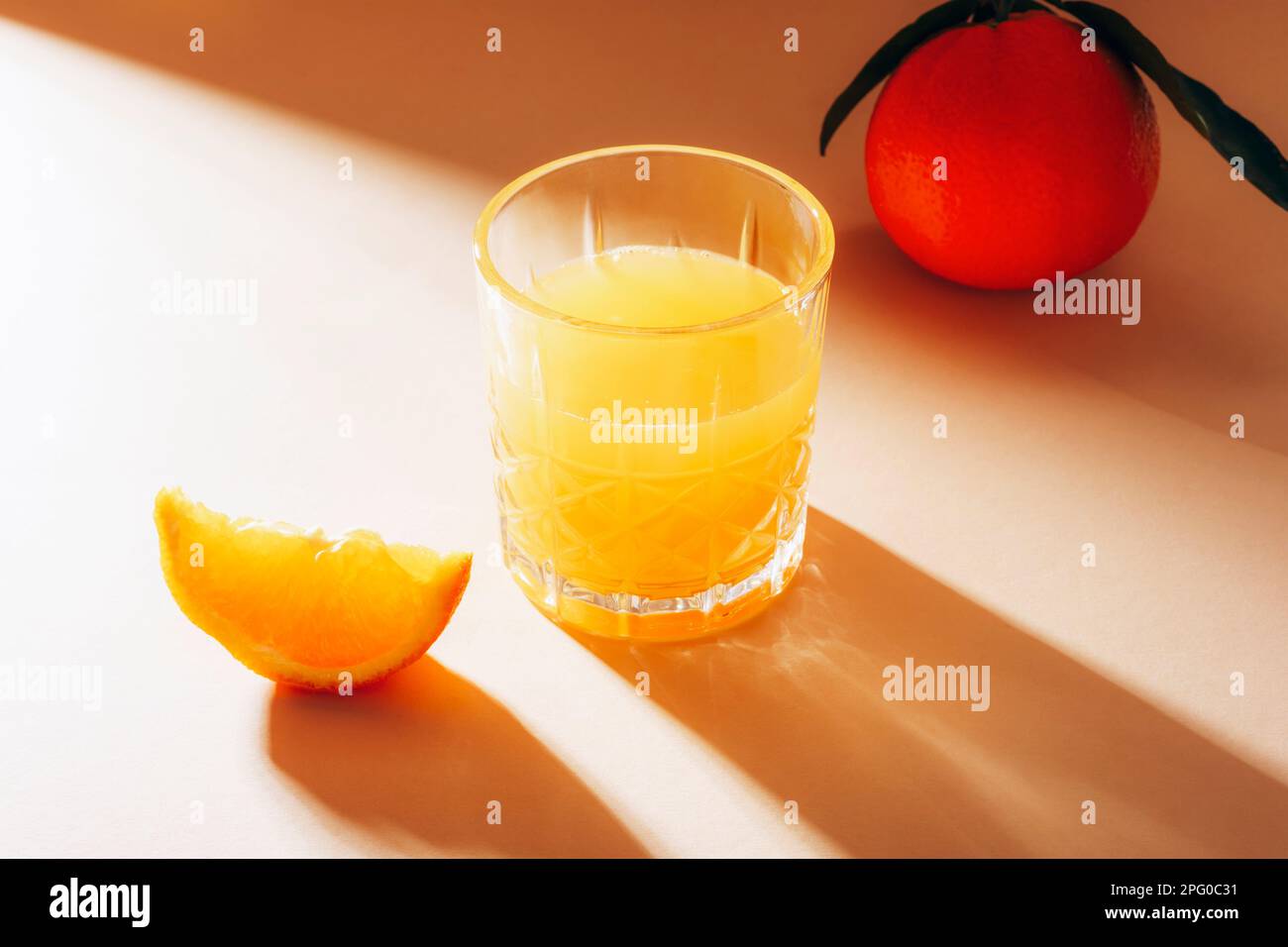 Un verre de jus d'orange et une tranche de fruits d'orange sur une table beige avec de longues ombres dures. Aliments végétaliens crus sains, concept de régime alimentaire. Gros plan. Banque D'Images