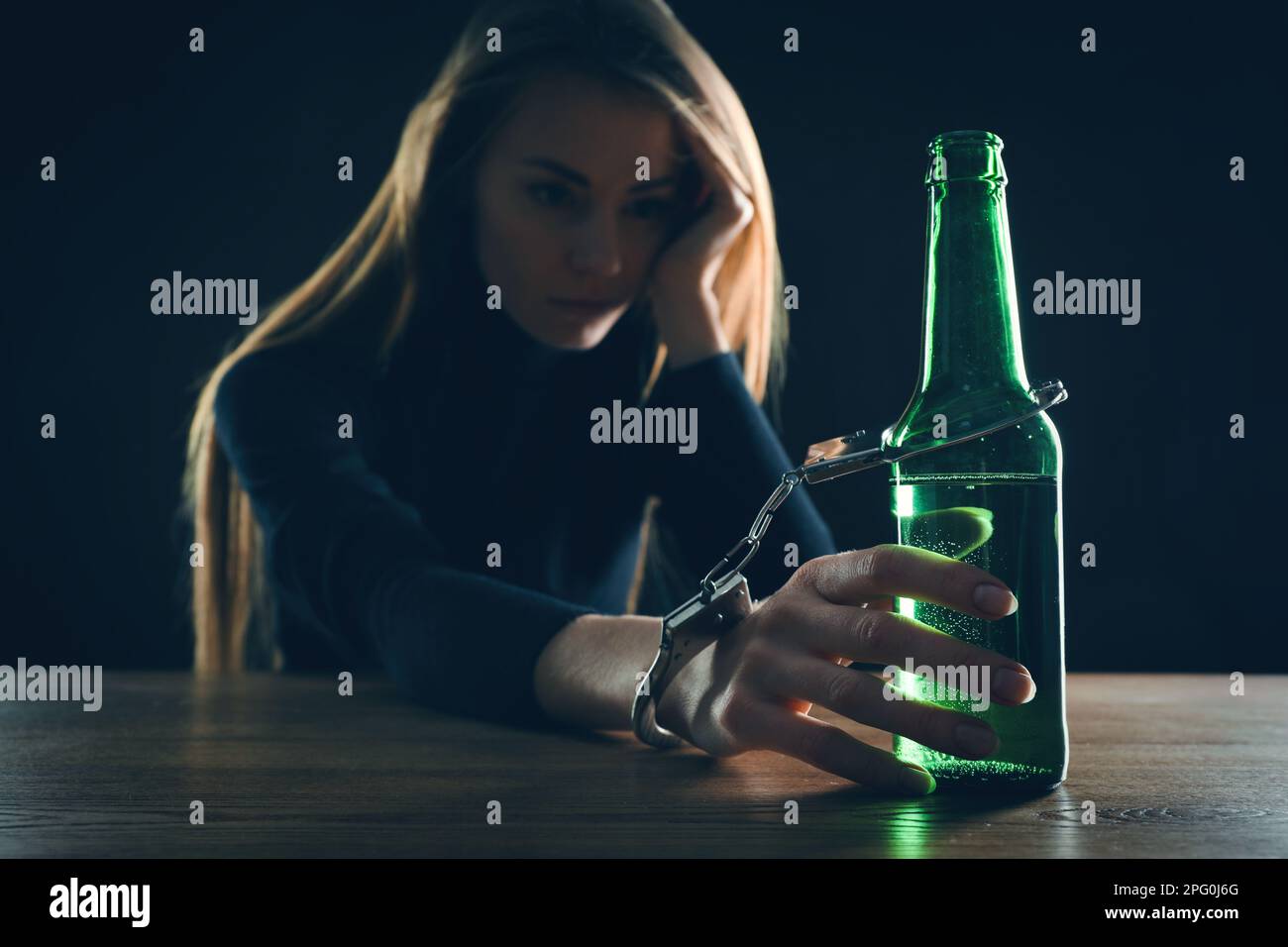 Dépendance à l'alcool. Femme menottée à une bouteille de bière à une table en bois sur fond noir, se concentrer sur la main Banque D'Images