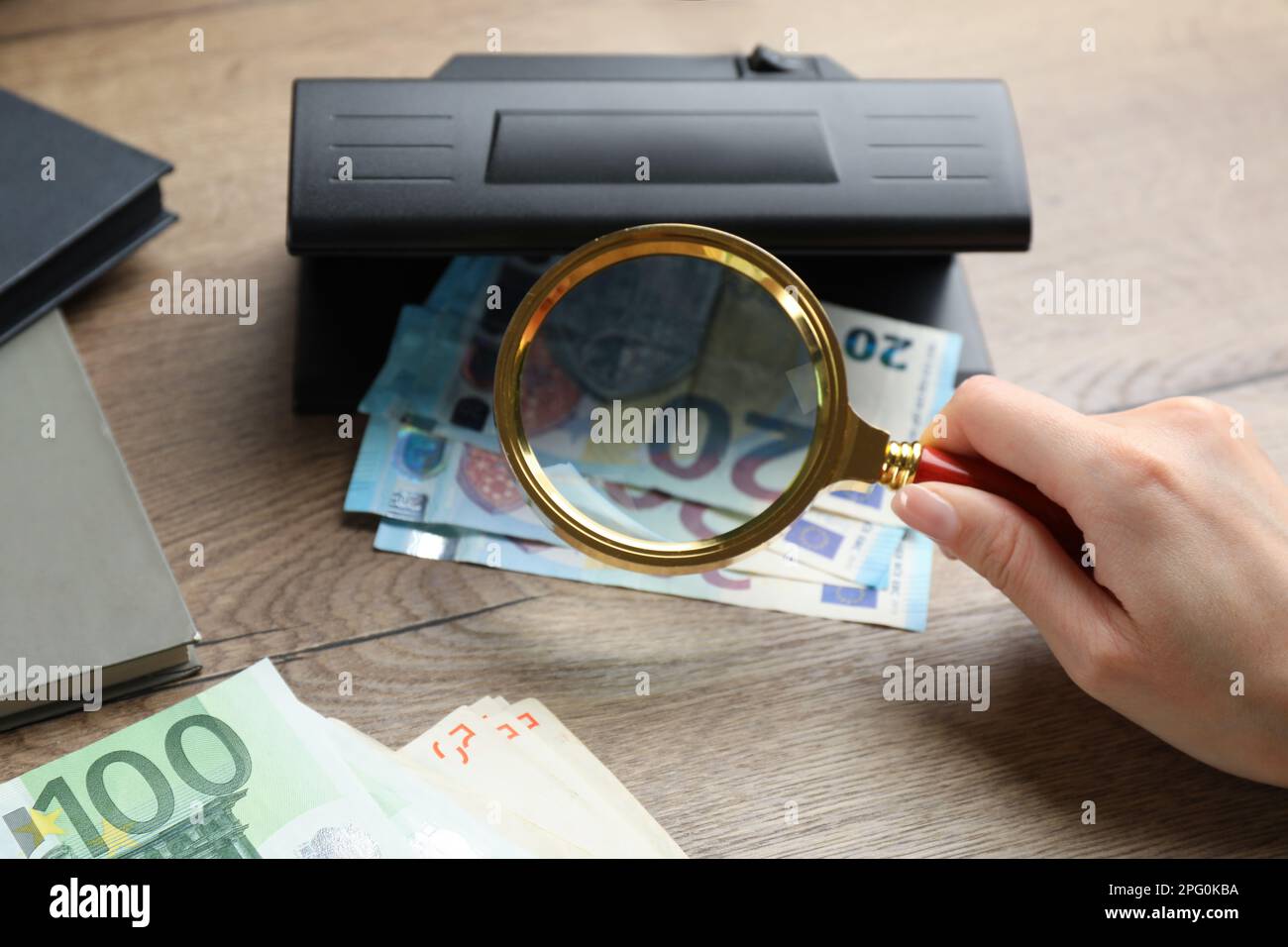 Femme vérifiant les billets en euros avec détecteur de devises et loupe à table en bois, gros plan. Appareil d'examen de l'argent Banque D'Images