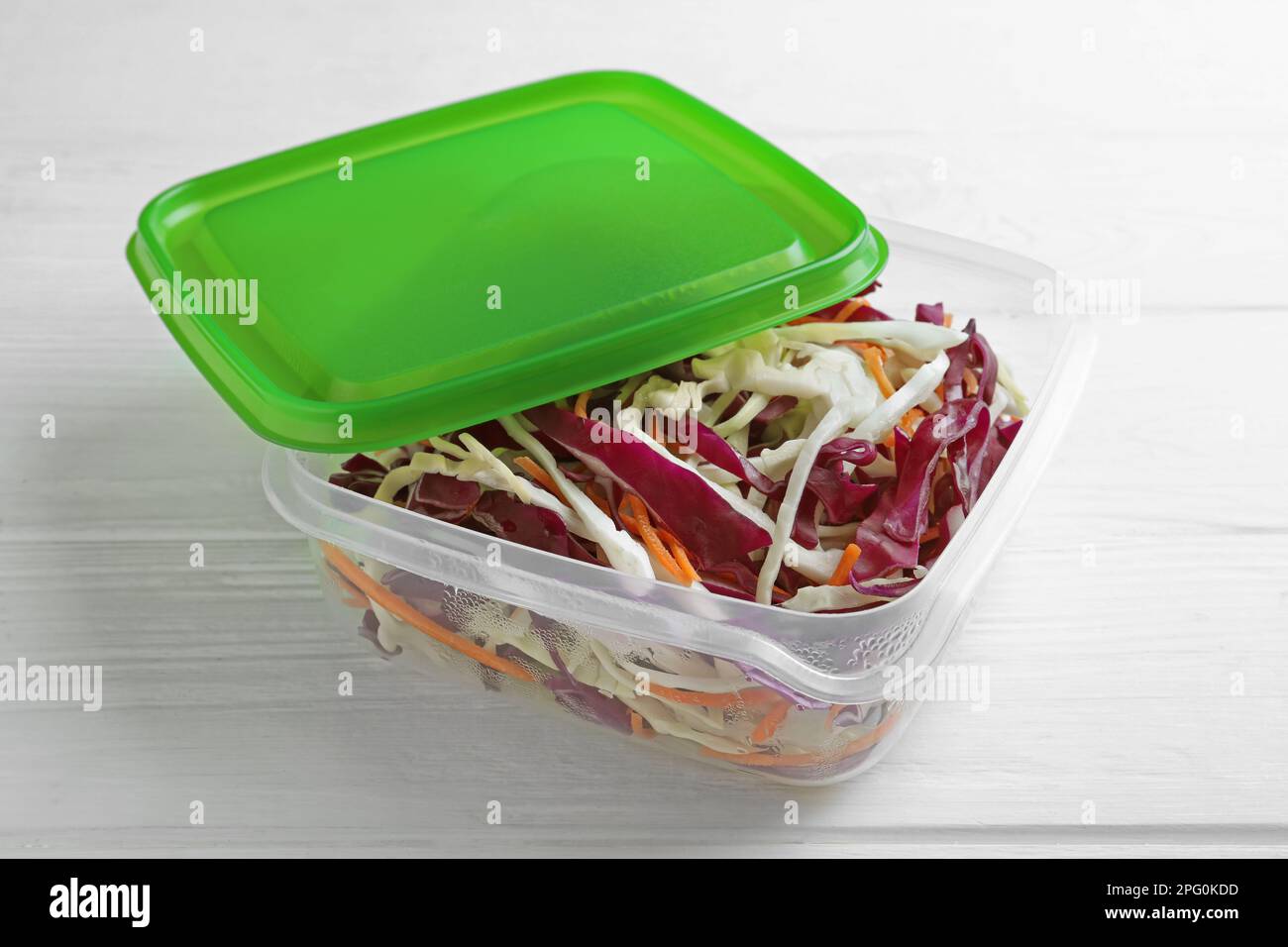 Salade de chou frais avec carotte déchiquetée dans un contenant en plastique sur table en bois blanc Banque D'Images