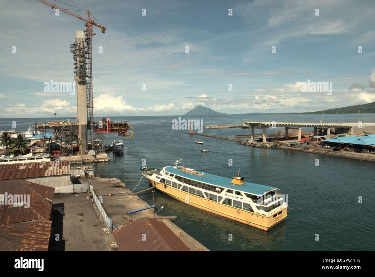 Vue sur la baie de Manado avec le mont Manado Tua en premier plan d'un ferry et d'une partie du pont Soekarno en construction dans la zone côtière de Manado, au nord de Sulawesi, en Indonésie. Banque D'Images