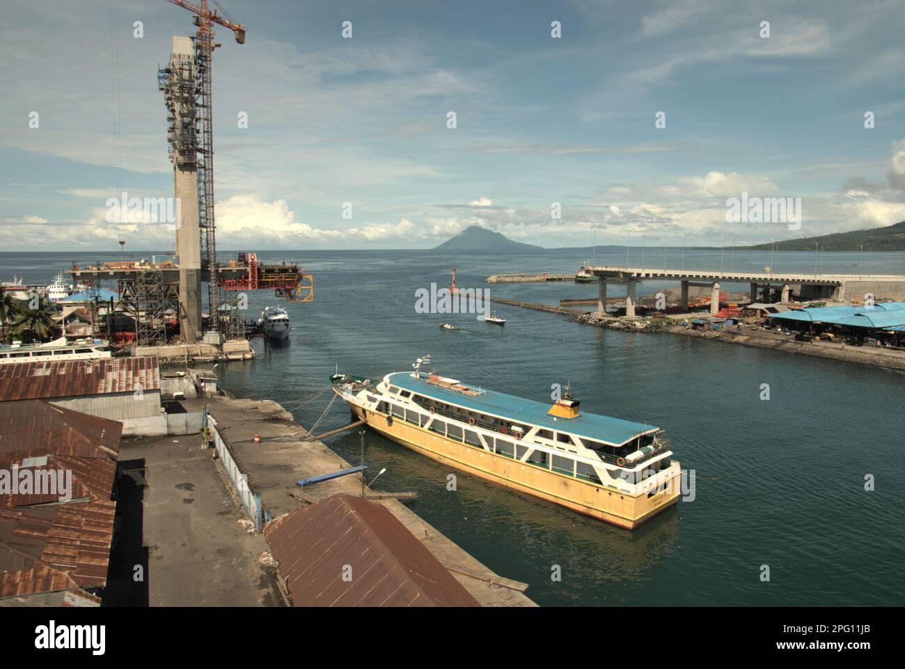 Vue sur la baie de Manado avec le mont Manado Tua en premier plan d'un ferry et d'une partie du pont Soekarno en construction dans la zone côtière de Manado, au nord de Sulawesi, en Indonésie. Banque D'Images