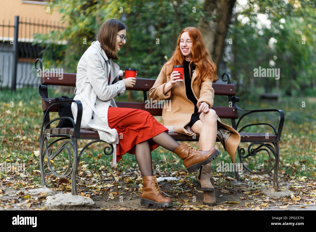 les filles s'amusent à s'asseoir avec des boissons chaudes dans le parc d'automne sur un banc Banque D'Images