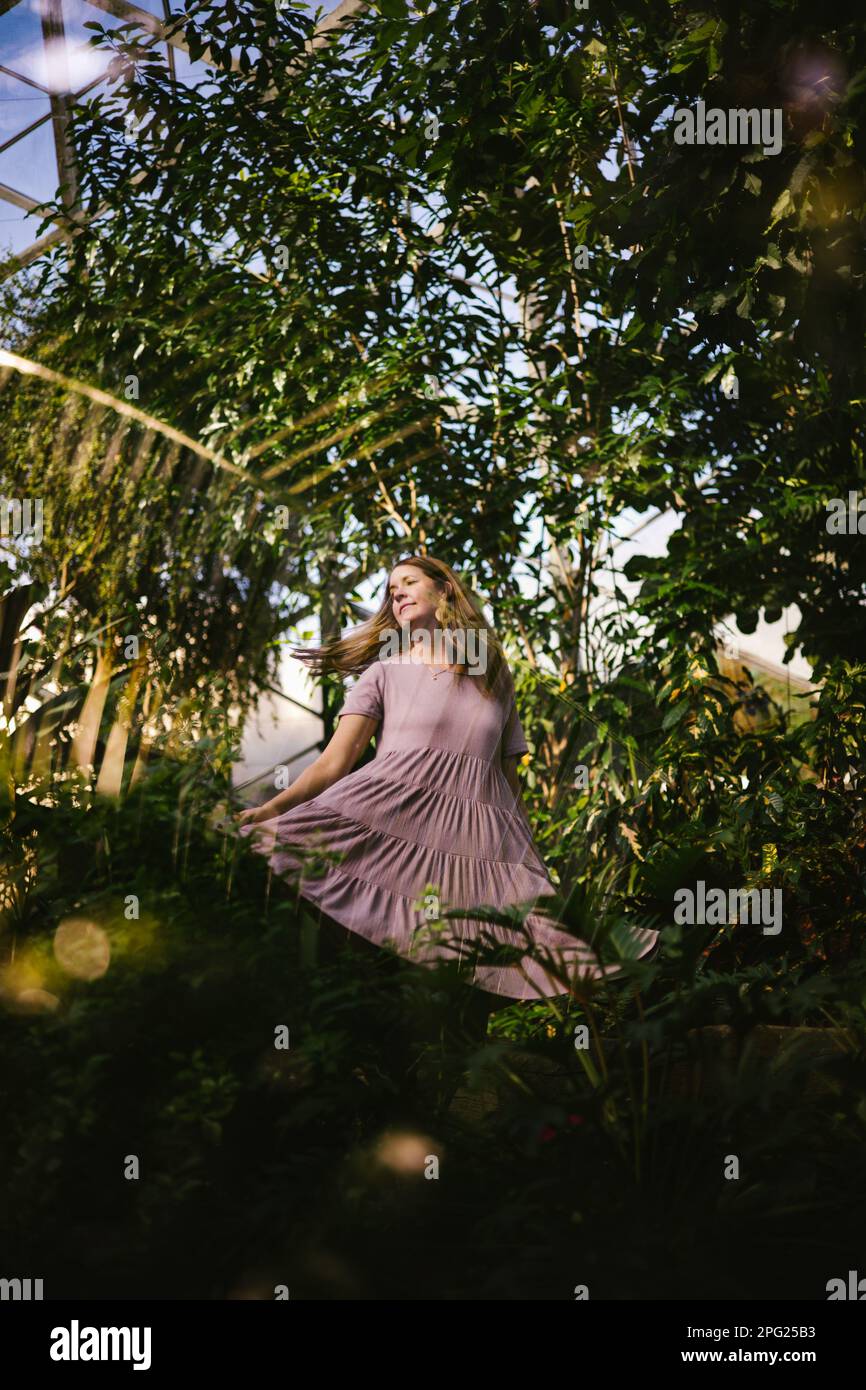 Femme brindilles en robe pourpre dans le jardin d'hiver de plantes tropicales Banque D'Images