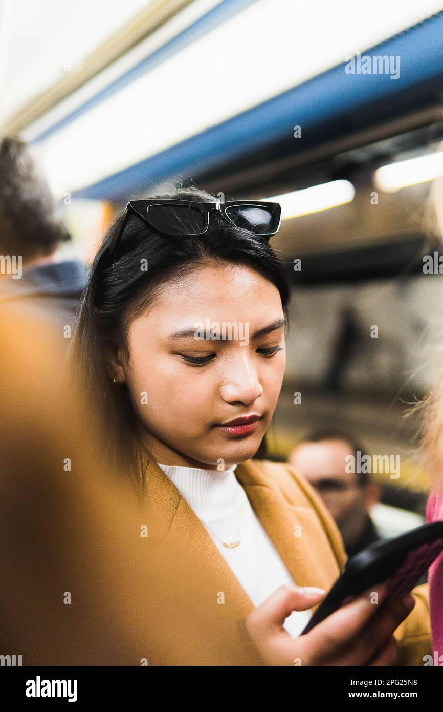 Fille asiatique sur le métro en utilisant le téléphone entouré de personnes Banque D'Images