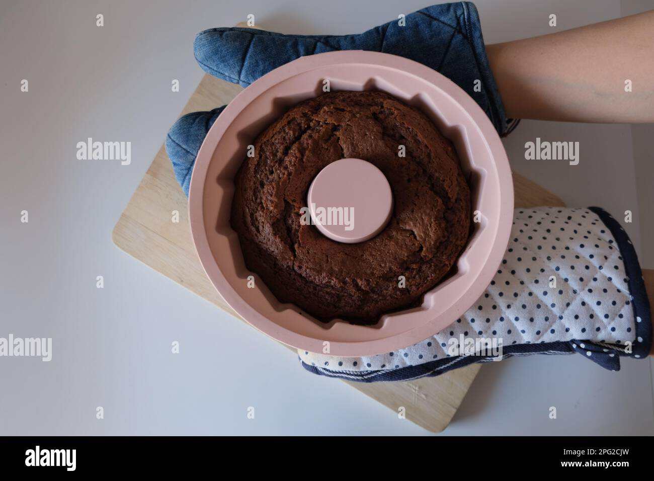 Gâteau cuit dans un moule en silicone, la femme met un gâteau de cacao dans un moule en silicone rond rose sur une planche à découper en bois dans la cuisine. La photo de concept de la nourriture. Banque D'Images