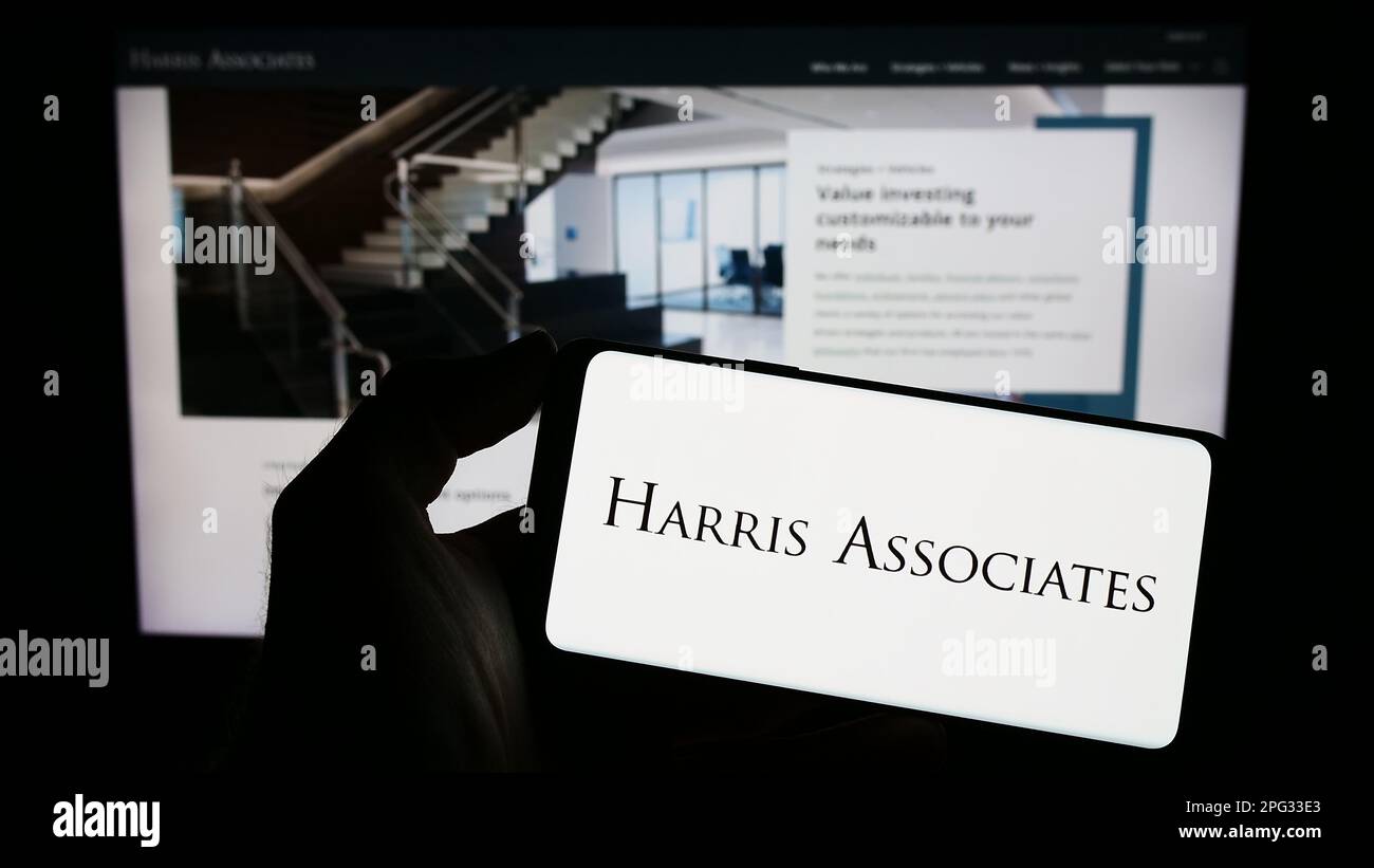 Personne tenant un téléphone mobile avec le logo de la société d'investissement américaine Harris Associates LP à l'écran en face de la page Web. Mise au point sur l'affichage du téléphone. Banque D'Images