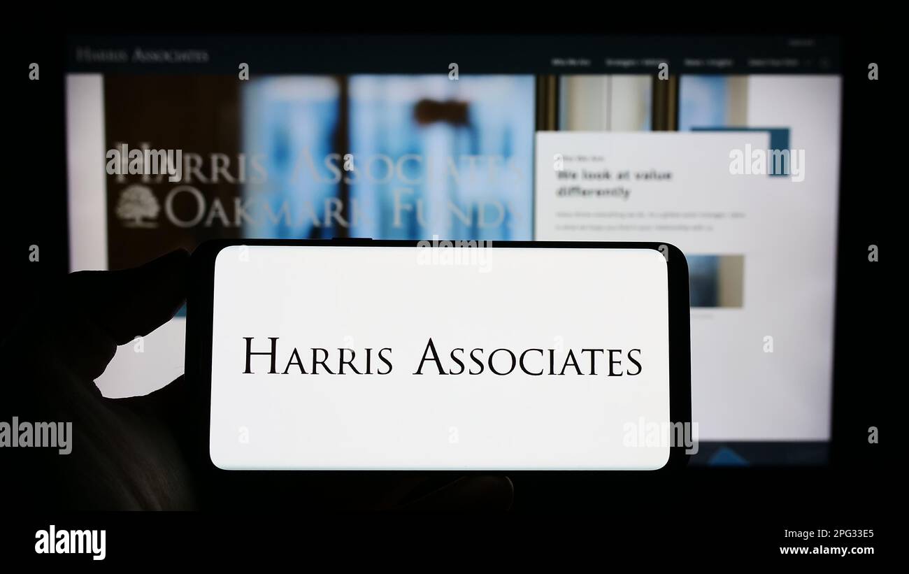 Personne tenant un téléphone portable avec le logo de la société d'investissement américaine Harris Associates L.P. à l'écran devant la page Web d'affaires. Mise au point sur l'affichage du téléphone. Banque D'Images