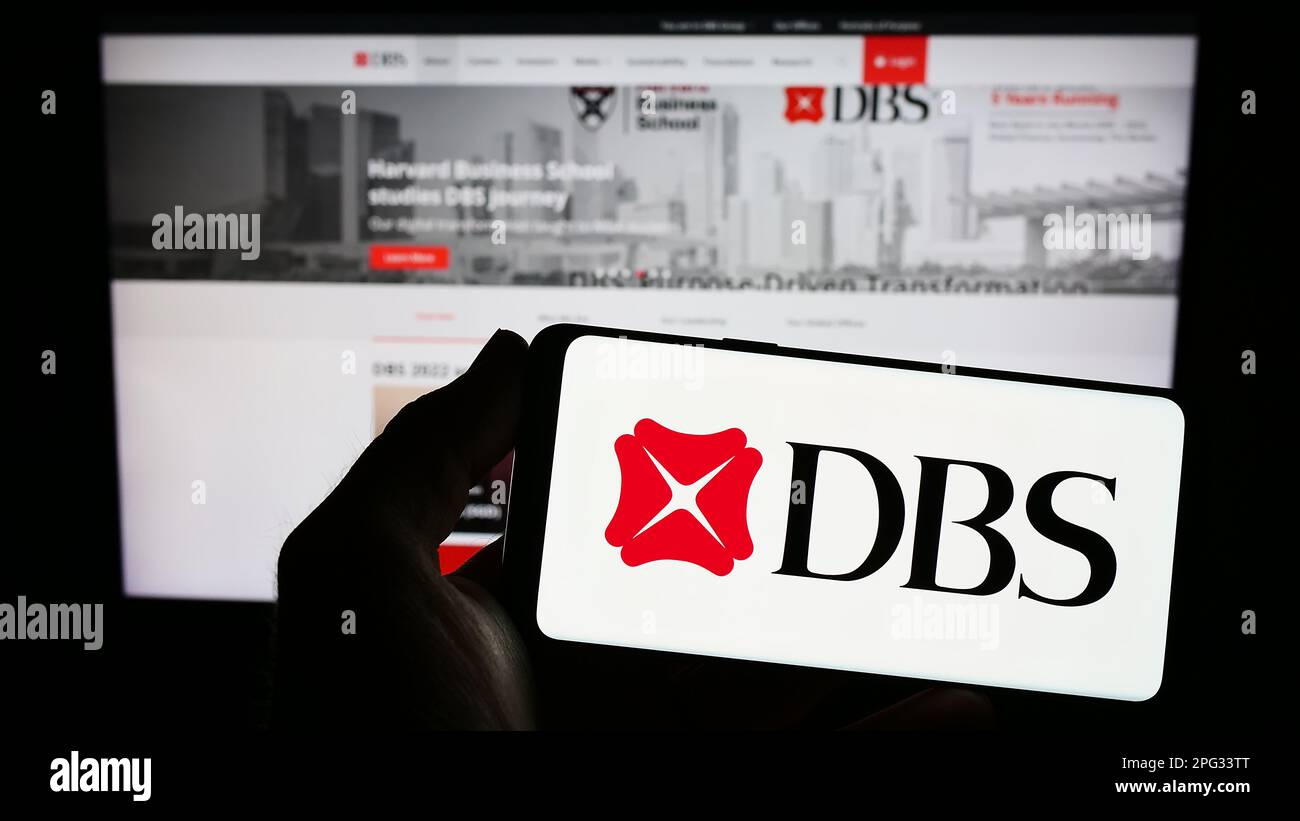 Personne tenant un smartphone avec le logo de la société financière Singapourienne DBS Bank Limited à l'écran devant le site Web. Mise au point sur l'affichage du téléphone. Banque D'Images
