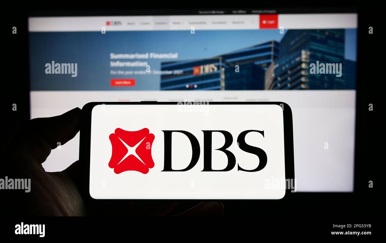 Personne tenant un téléphone portable avec le logo de la société financière Singapourienne DBS Bank Limited à l'écran devant la page Web. Mise au point sur l'affichage du téléphone. Banque D'Images