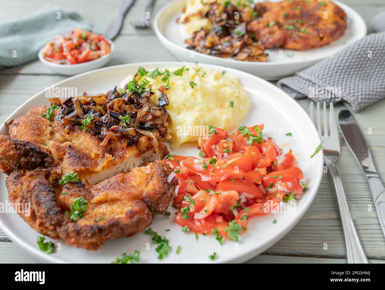 Côtelettes panées avec oignon rôti, purée de pommes de terre et salade de tomates sur une assiette. Banque D'Images