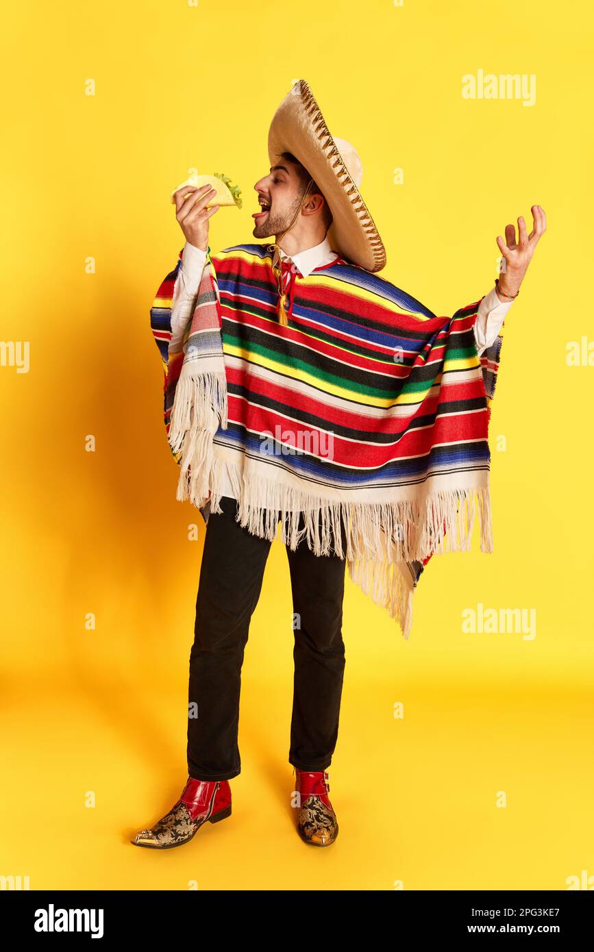 Portrait d'un jeune homme en vêtements colorés, poncho et sombrero posant,  mangeant du taco sur fond jaune de studio Photo Stock - Alamy