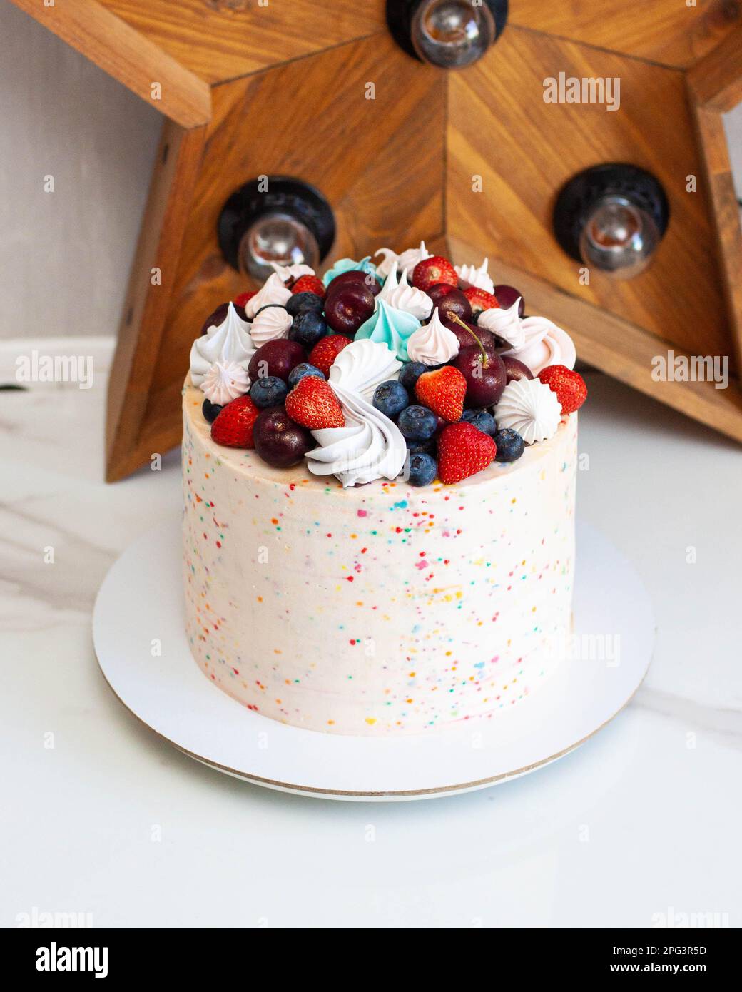 Joyeux gâteau d'anniversaire avec des saupoudriers, des cerises, des fraises, des bleuets et des meringues Banque D'Images
