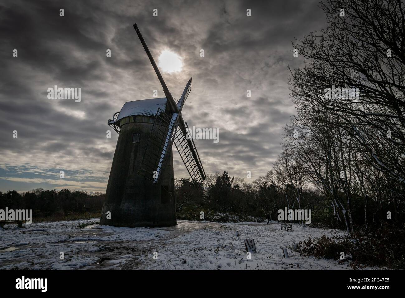 Birkenhead, Royaume-Uni - 10 mars 2023: Moulin à vent Bidston silhoueté par un soleil bas qui se couche à travers les nuages sur un paysage enneigé. Datant de 1800, c'est un Banque D'Images