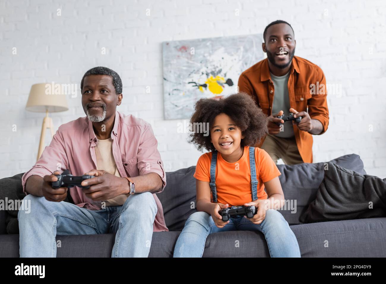 KIEV, UKRAINE - 17 JUILLET 2021 : gamin afro-américain joyeux jouant au jeu vidéo avec le père et le grand-père à la maison Banque D'Images