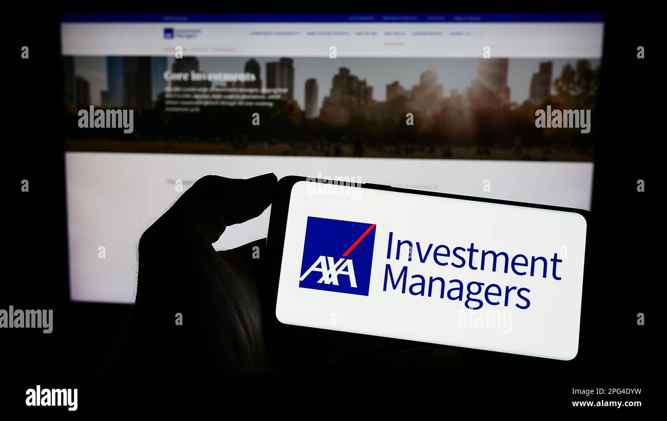 Personne détenant un téléphone portable avec logo de la société d'investissement AXA Investment Managers à l'écran en face de la page web business. Mise au point sur l'affichage du téléphone. Banque D'Images