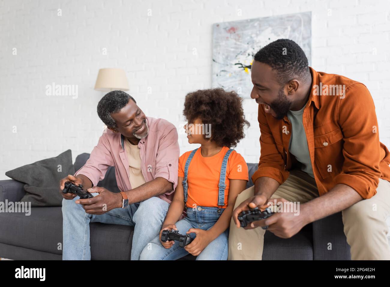 KIEV, UKRAINE - 17 JUILLET 2021: Sourire afro-américain grand-parent jouant le jeu vidéo avec enfant et fils à la maison Banque D'Images