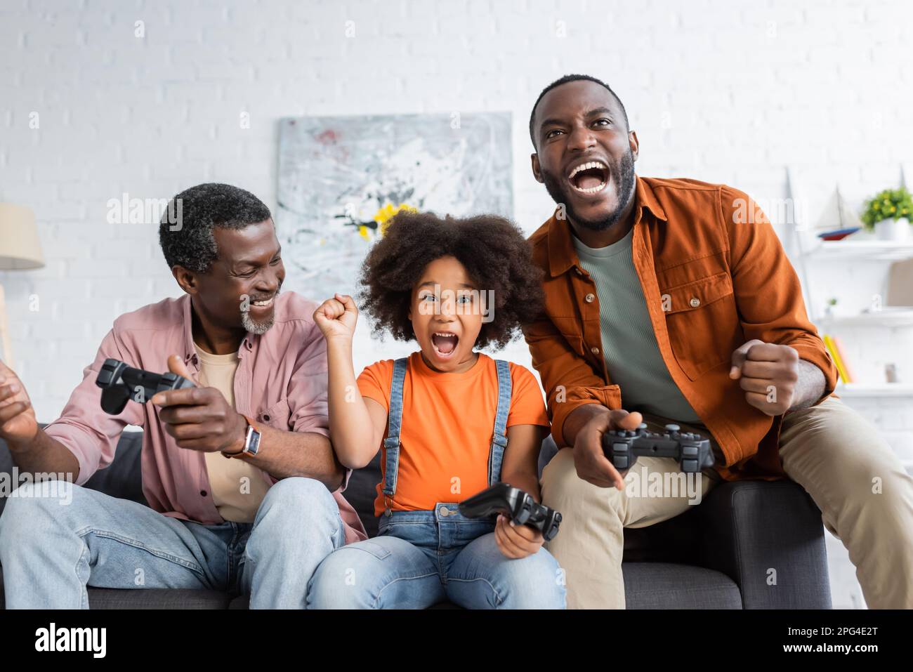 KIEV, UKRAINE - 17 JUILLET 2021 : une fille et un père afro-américains enthousiastes tenant des manettes près du grand-père à la maison Banque D'Images