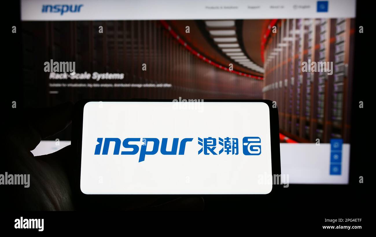 Personne tenant le téléphone portable avec le logo de la société de technologie de l'information Inspur Group sur l'écran en face de la page Web d'affaires. Mise au point sur l'affichage du téléphone. Banque D'Images