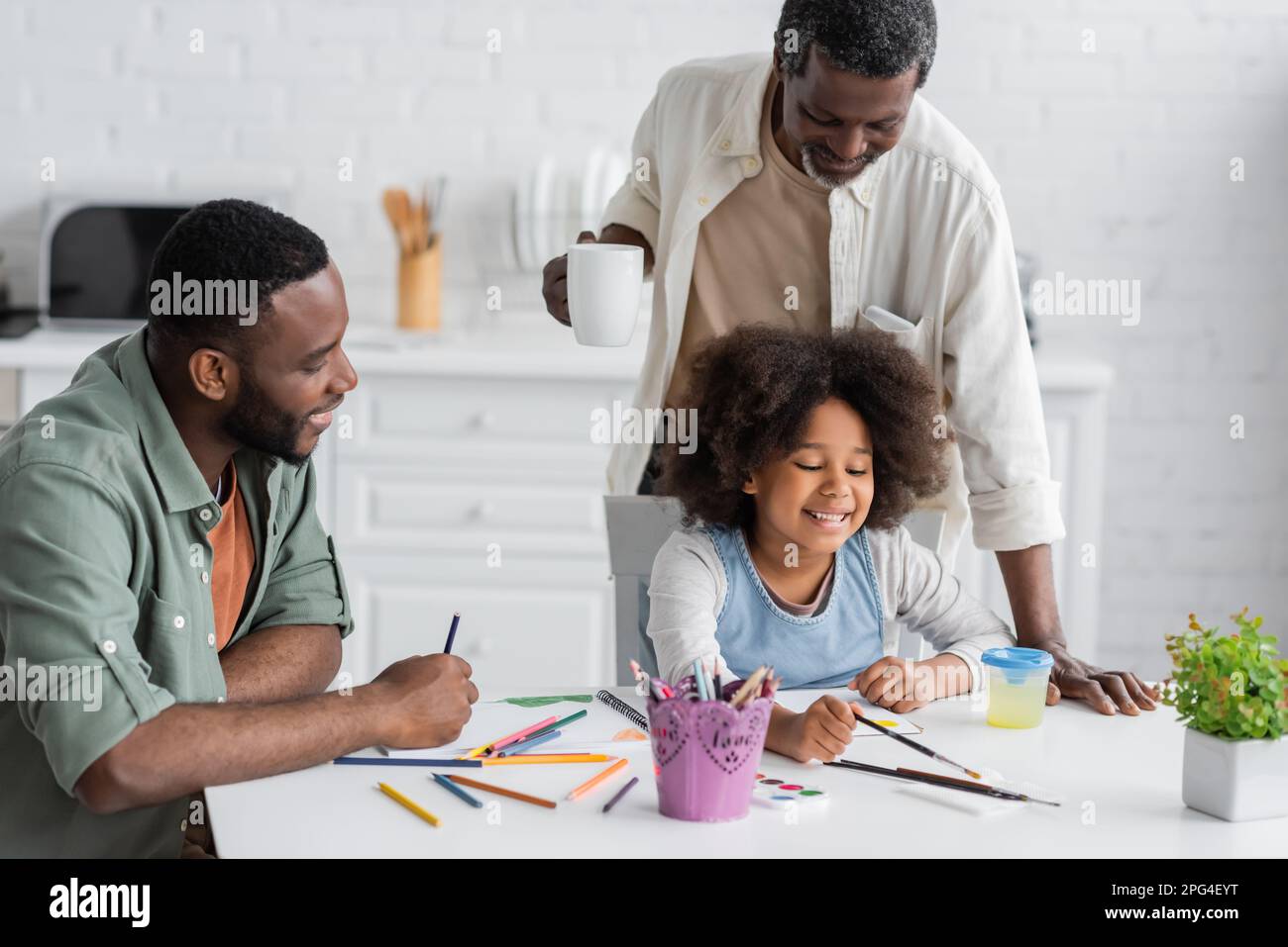 Homme américain africain positif assis près de la peinture de fille et le père tenant une tasse de café à la maison, image de stock Banque D'Images