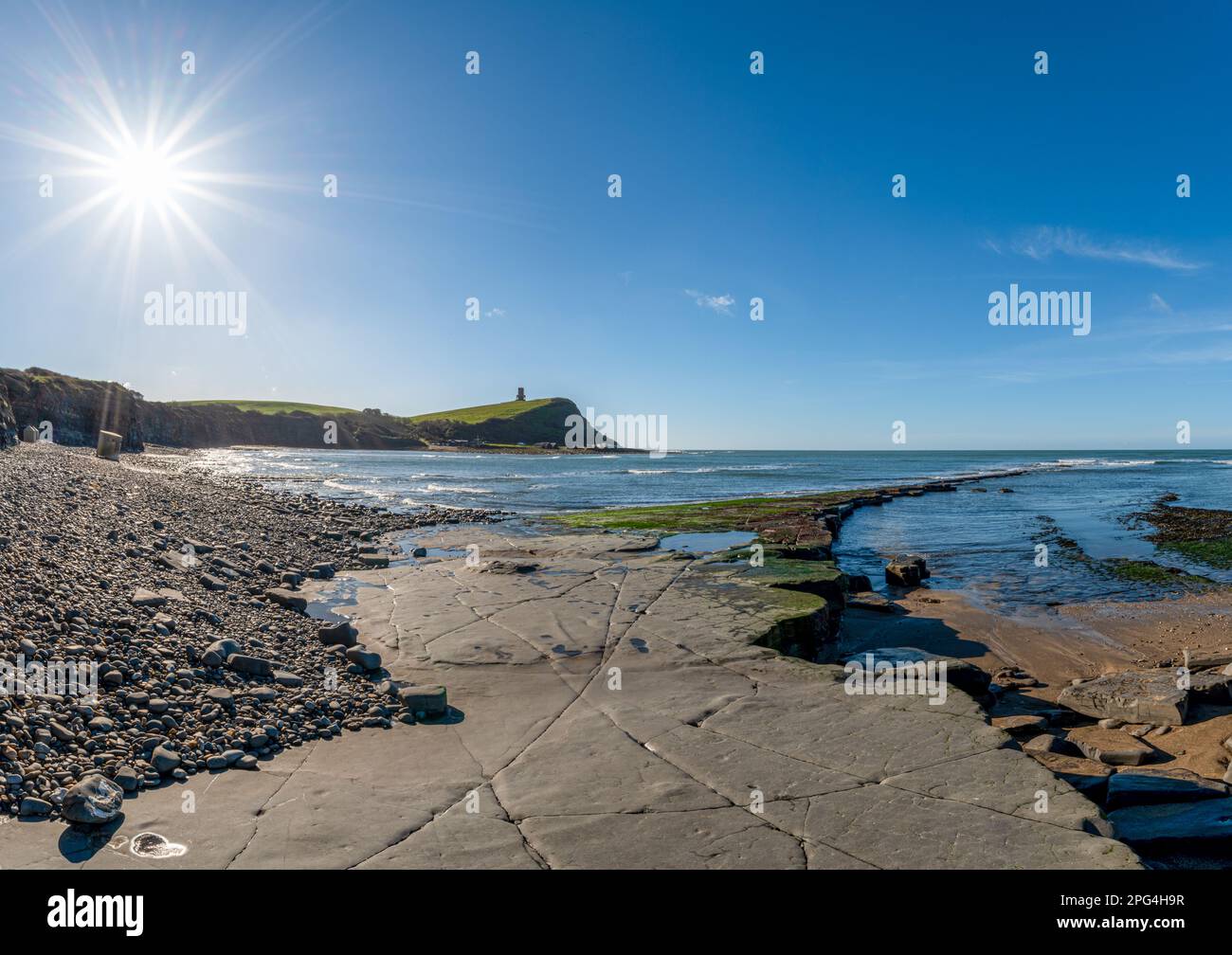 Scène de la baie de Kimmeridge avec la formation d'argile de Kimmeridge allant vers la mer et sunstar sur un ciel bleu clair avec WW2 pilbox de type 25 et tour de clavell Banque D'Images