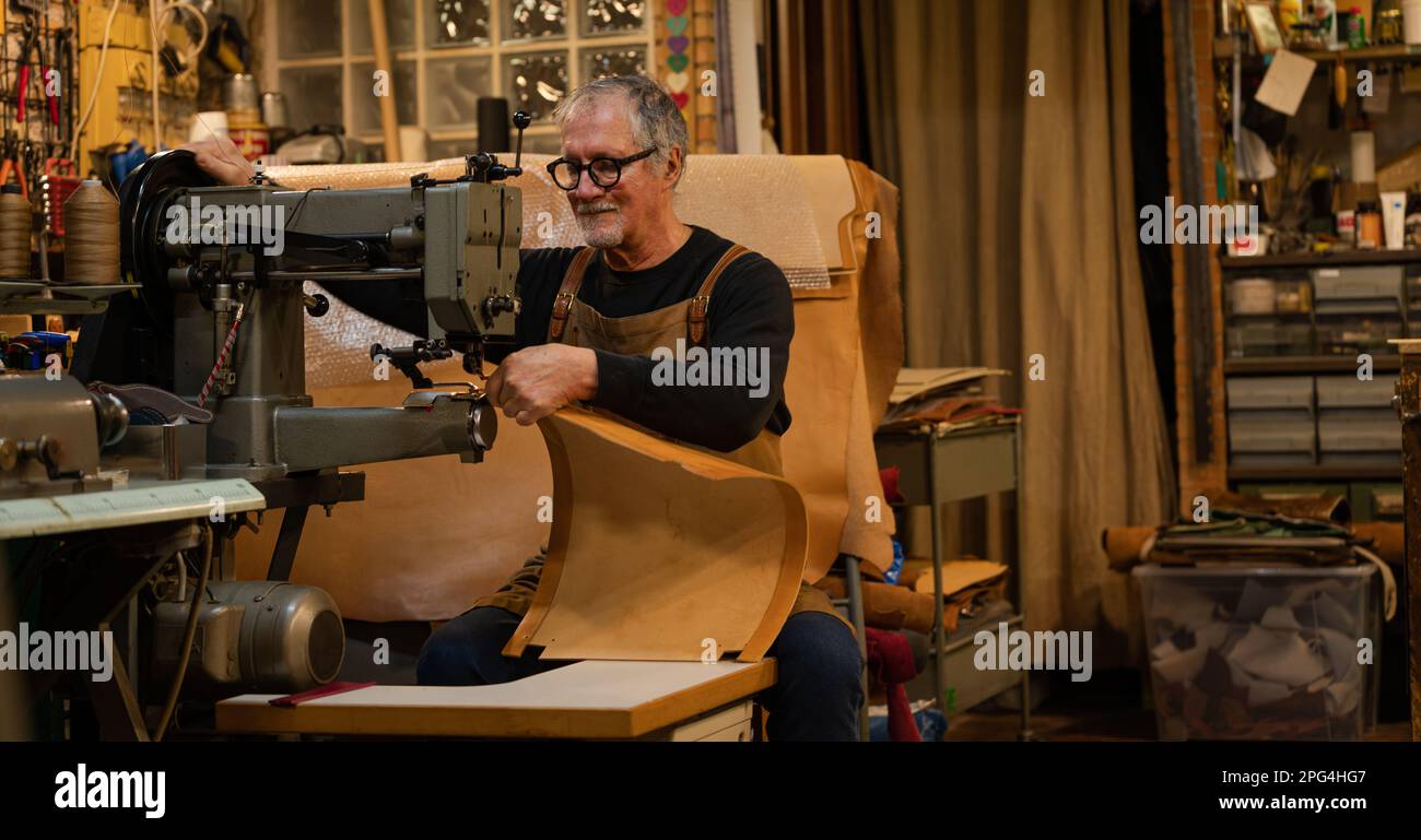 tanner senior assis couture de cuir panneau arrière avec une machine à coudre pour une chaise faite par lui dans l'atelier Banque D'Images