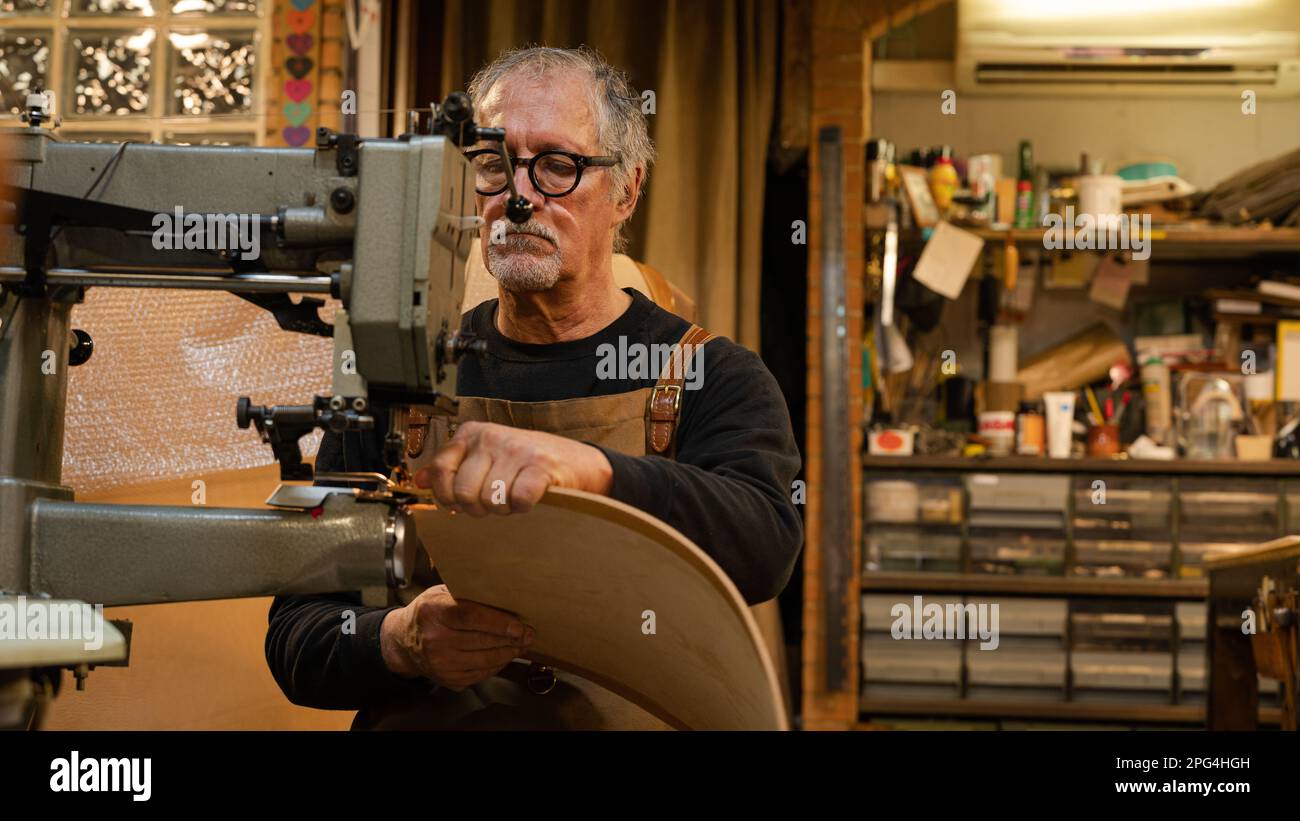 vue en face d'un artisan en cuir assis tout en coudre le dos d'une chaise faite par lui dans l'atelier, rome, italie Banque D'Images