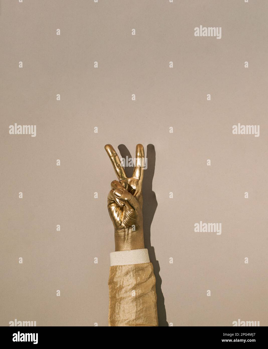 Main peinte en or avec deux doigts relevés. Symbole de paix, force, combat, victoire et lettre V sur fond gris. Banque D'Images