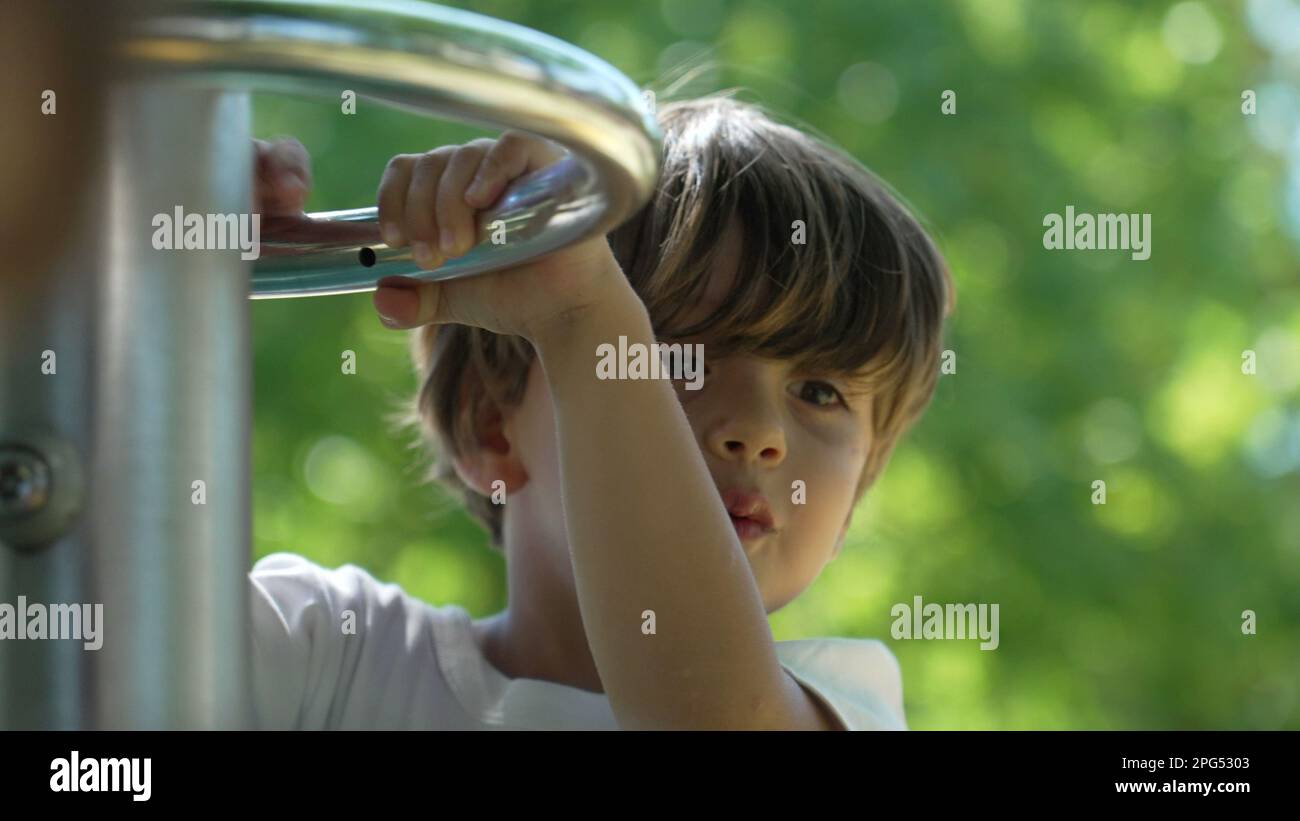 Enfant heureux sans souci tenant sur le terrain de jeu, les barres du carrousel se ferment face et les mains à l'extérieur au parc Banque D'Images