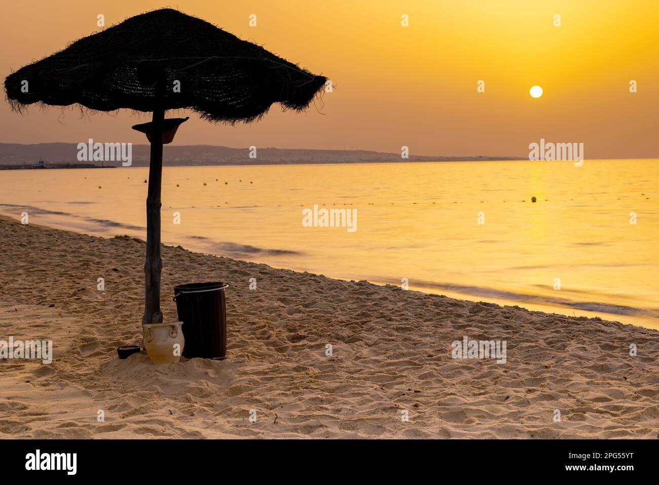 Découvrez la beauté sereine d'une plage tunisienne au coucher du soleil, avec de douces vagues qui s'écrasent contre la rive et le parapluie en bois qui s'étend sous un Banque D'Images