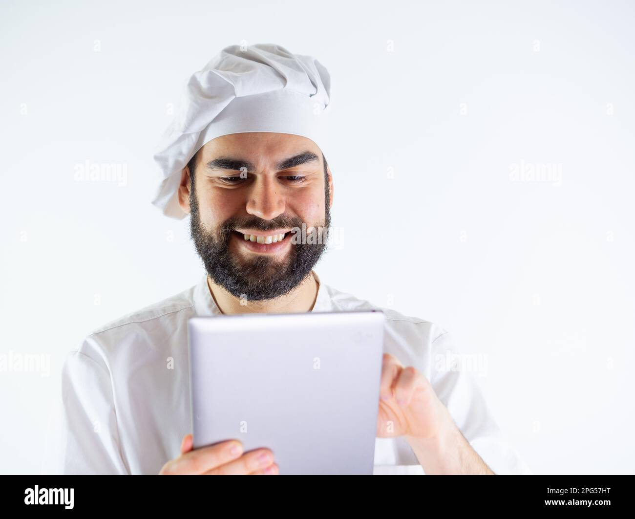 Jeune chef masculin utilisant une tablette, lisant une recette. Isolé sur un fond blanc Banque D'Images
