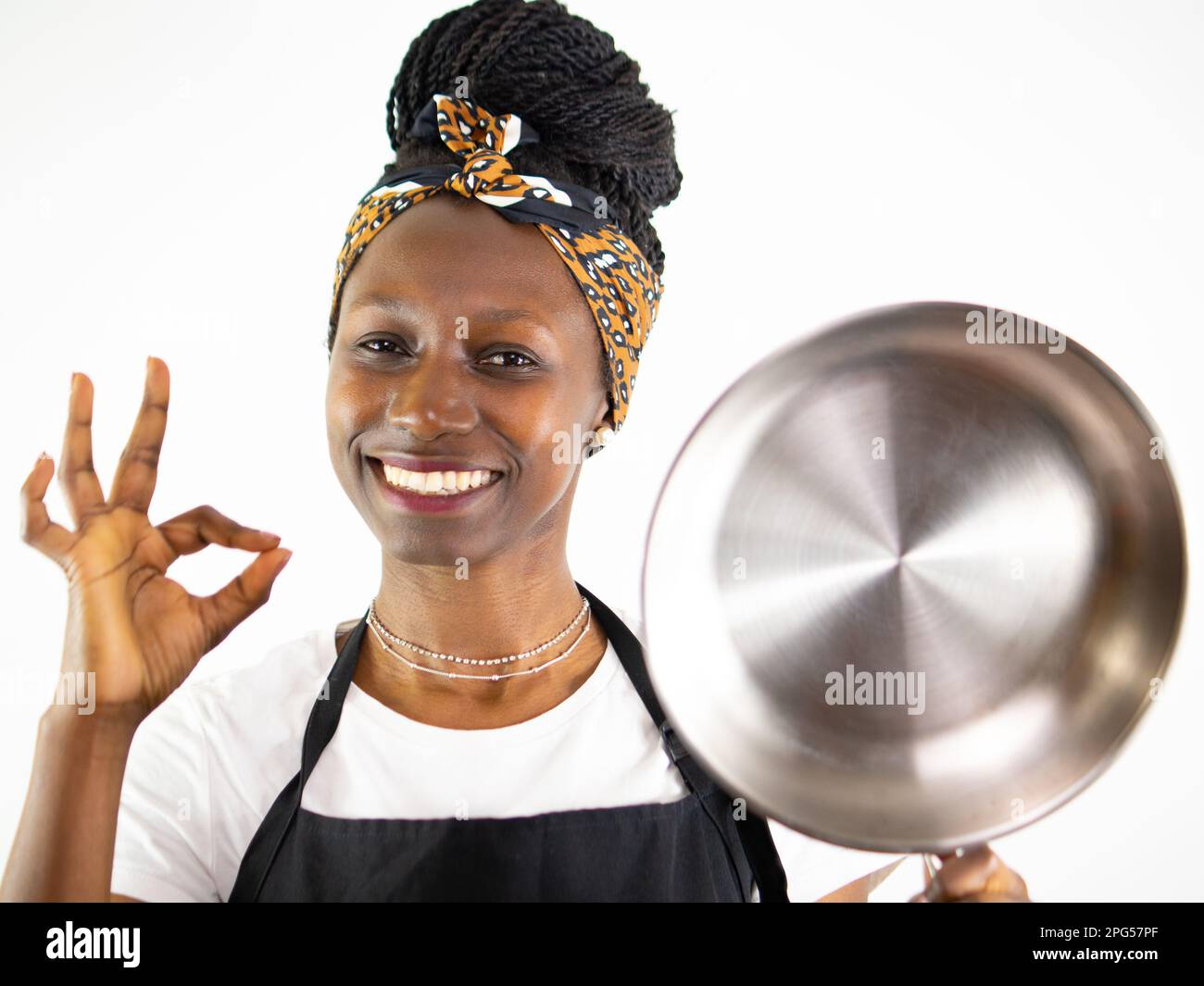 Jeune femme chef montrant une casserole en acier inoxydable tout en souriant et regardant l'appareil photo. Isolé sur un fond blanc Banque D'Images