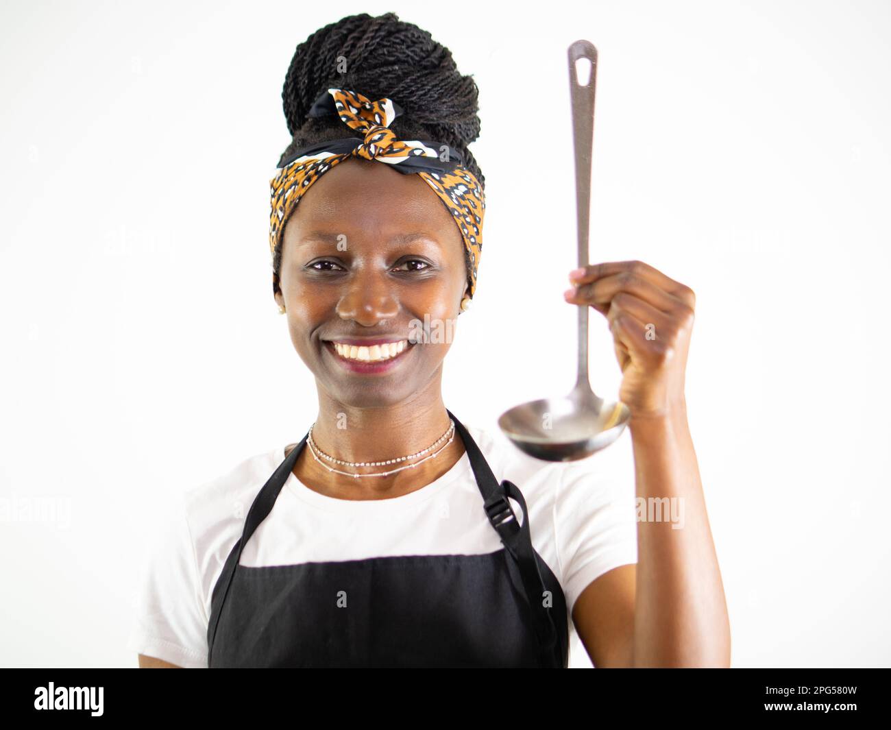 Jeune femme chef montrant une louche en métal tout en souriant et regardant l'appareil photo. Isolé sur un fond blanc Banque D'Images