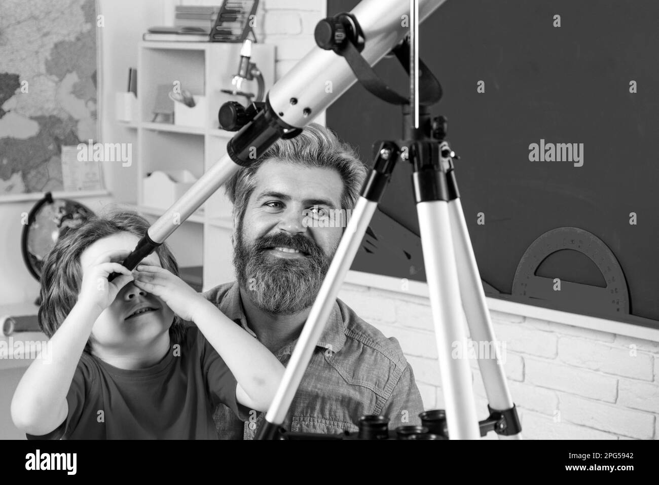 Père enseignant son à l'aide d'un télescope. Portrait de l'élève de l'école primaire étudier à l'intérieur. Fête des pères. Père et fils heureux. Banque D'Images