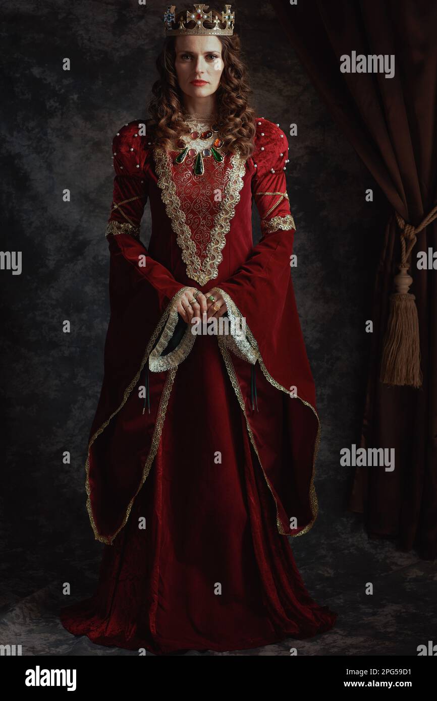 reine médiévale en robe rouge avec couronne sur fond gris foncé. Banque D'Images