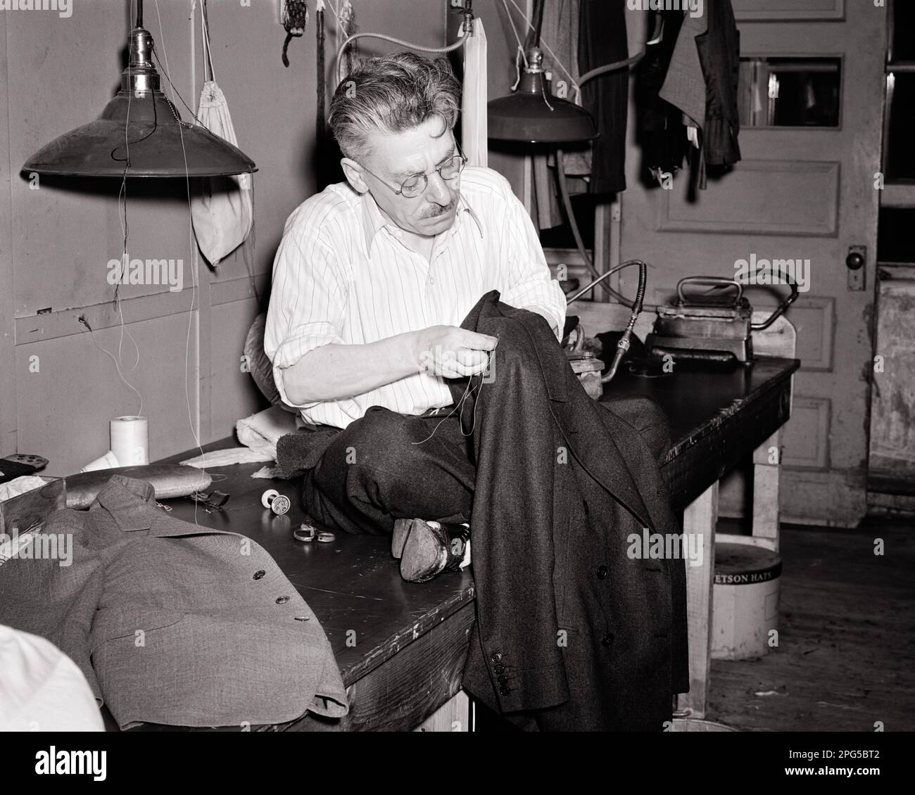 1940S HOMME D'ÂGE MOYEN UN TAILLEUR ASSIS AU-DESSUS D'UN COMPTOIR DANS UNE BOUTIQUE COUTURE D'UNE VESTE DE COSTUME D'HOMME - C2028 HAR001 HARS PROFESSION ARTISANAT B&W D'ÂGE MOYEN COMPÉTENCES D'HOMME D'ÂGE MOYEN COMPÉTENCES D'OCCUPATION SERVICE CLIENT PERSONNALISÉ CARRIÈRES MÉTIERS D'ARTISANAT D'HOMME HOMME HOMME ORIGINE ETHNIQUE CAUCASIENNE NOIR ET BLANC HAR001 ANCIENNE COUTURE Banque D'Images