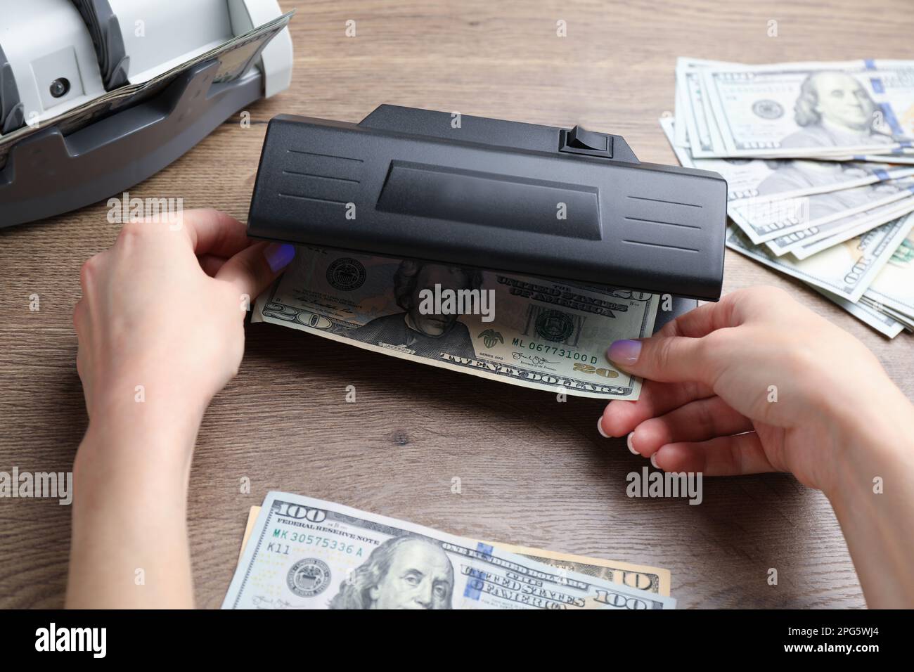 Femme vérifiant le billet de dollar avec détecteur de monnaie à la table en bois, gros plan. Appareil d'examen de l'argent Banque D'Images