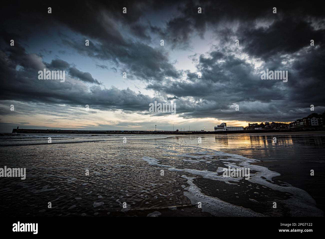 La marée recule à la plage de Sunny Sands à Folkestone au crépuscule. Les Stormclouds se déplacent sur le ciel, tandis que le dernier coucher de soleil silhouette les bâtiments. Banque D'Images